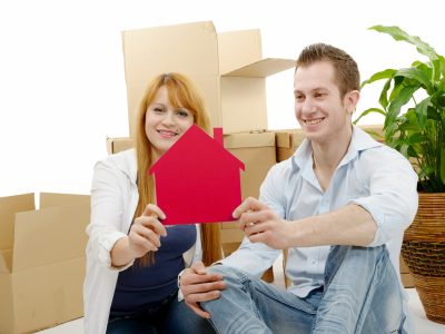 smiling young couple sitting after moving house, holding red house model